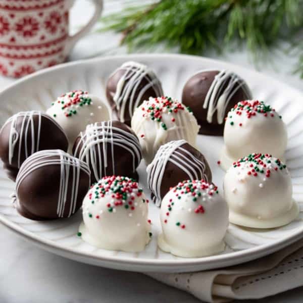 Chocolate-covered peanut butter balls topped with red and green sprinkles on a white plate.