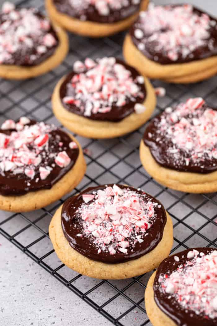 Peppermint cookies topped with chocolate ganache and crushed candy canes on a wire rack.