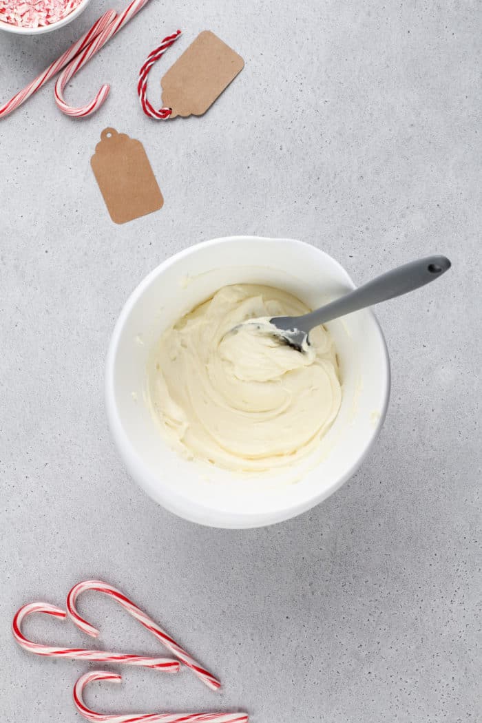 Bowl of cream cheese frosting on a countertop next to mini candy canes.