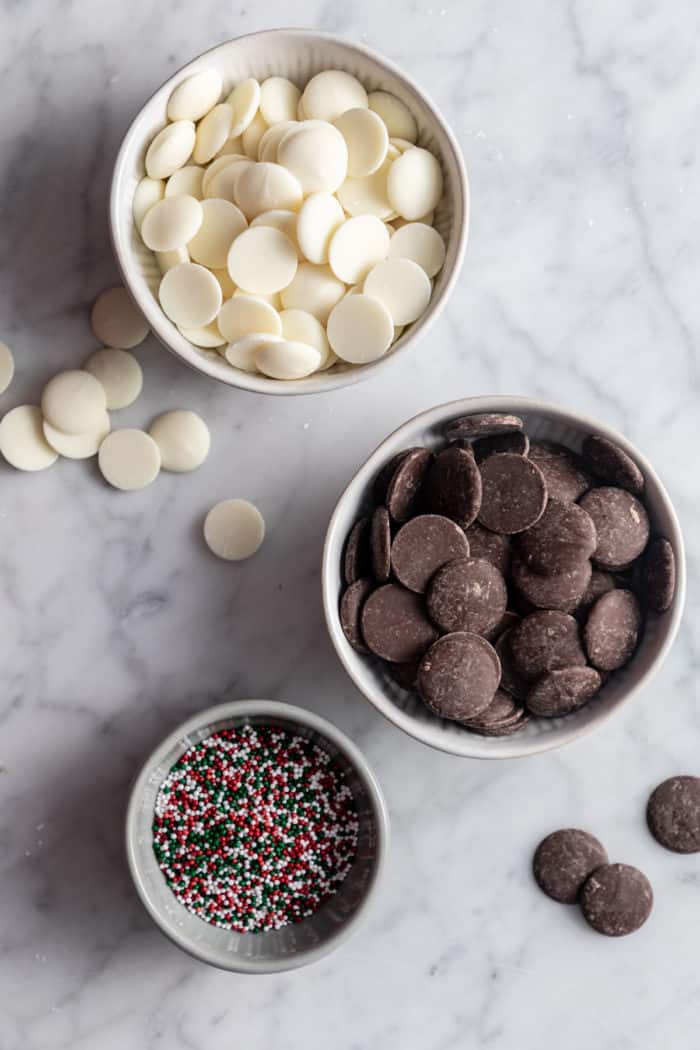 Chocolate-covered peanut butter balls topped with red and green sprinkles on a white plate.