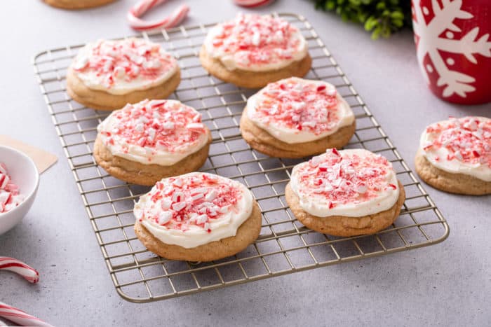 Wire rack filled with peppermint cookies frosted with cream cheese frosting and topped with crushed candy canes.