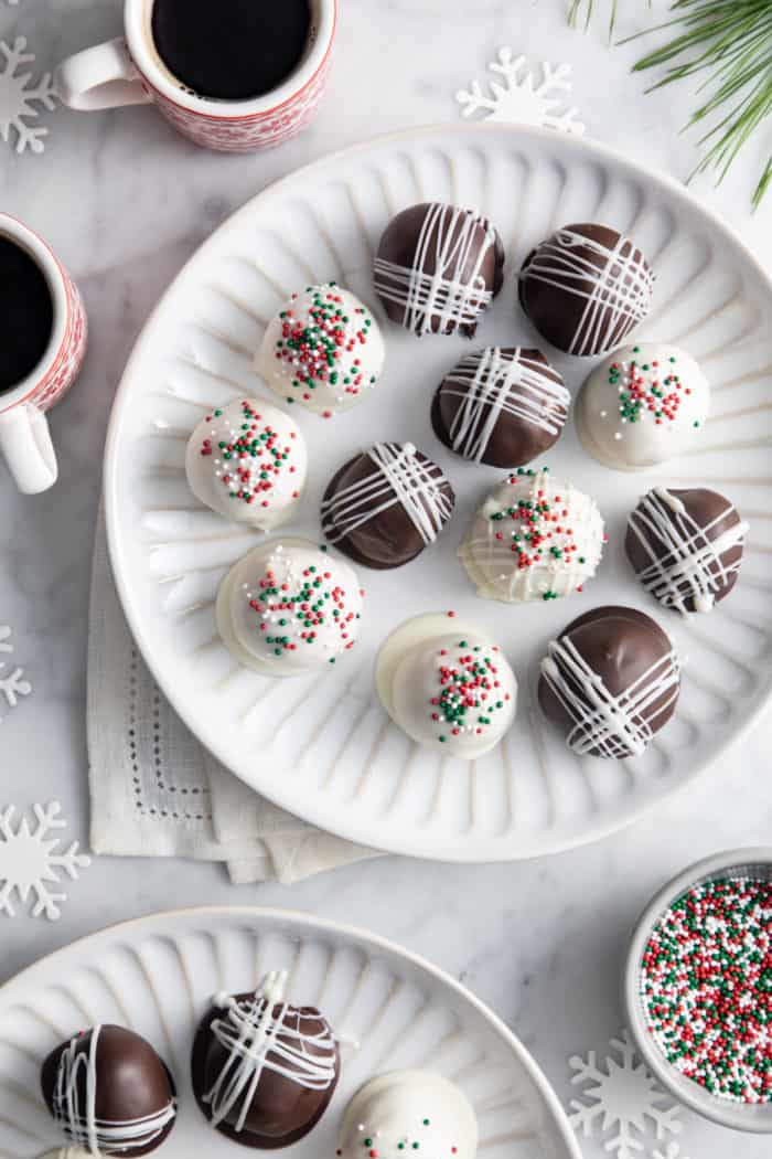 Overhead view of white plates filled with chocolate-covered peanut butter balls next to mugs of coffee.