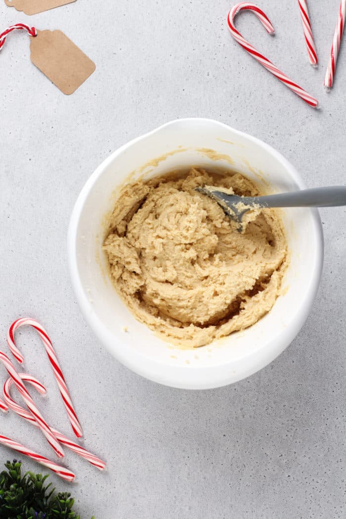 Peppermint cookie dough being stirred with a spatula in a white mixing bowl.