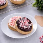 Two peppermint cookies – one topped with cream cheese frosting and one topped with chocolate ganache – on a white plate.