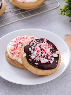 Two peppermint cookies – one topped with cream cheese frosting and one topped with chocolate ganache – on a white plate.