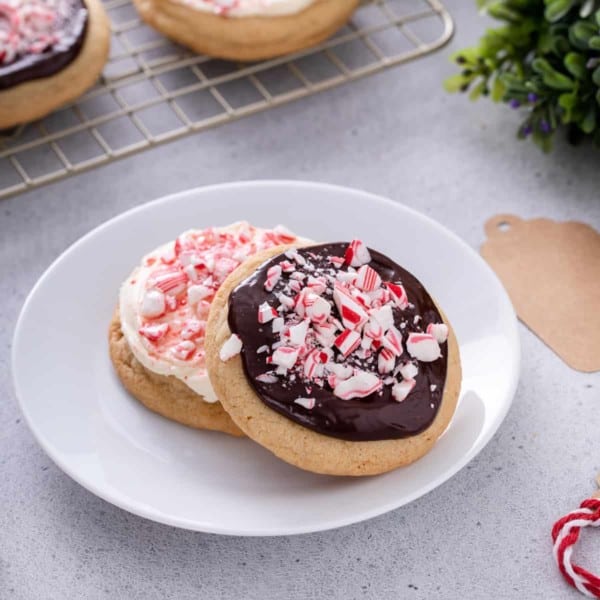 Two peppermint cookies – one topped with cream cheese frosting and one topped with chocolate ganache – on a white plate.
