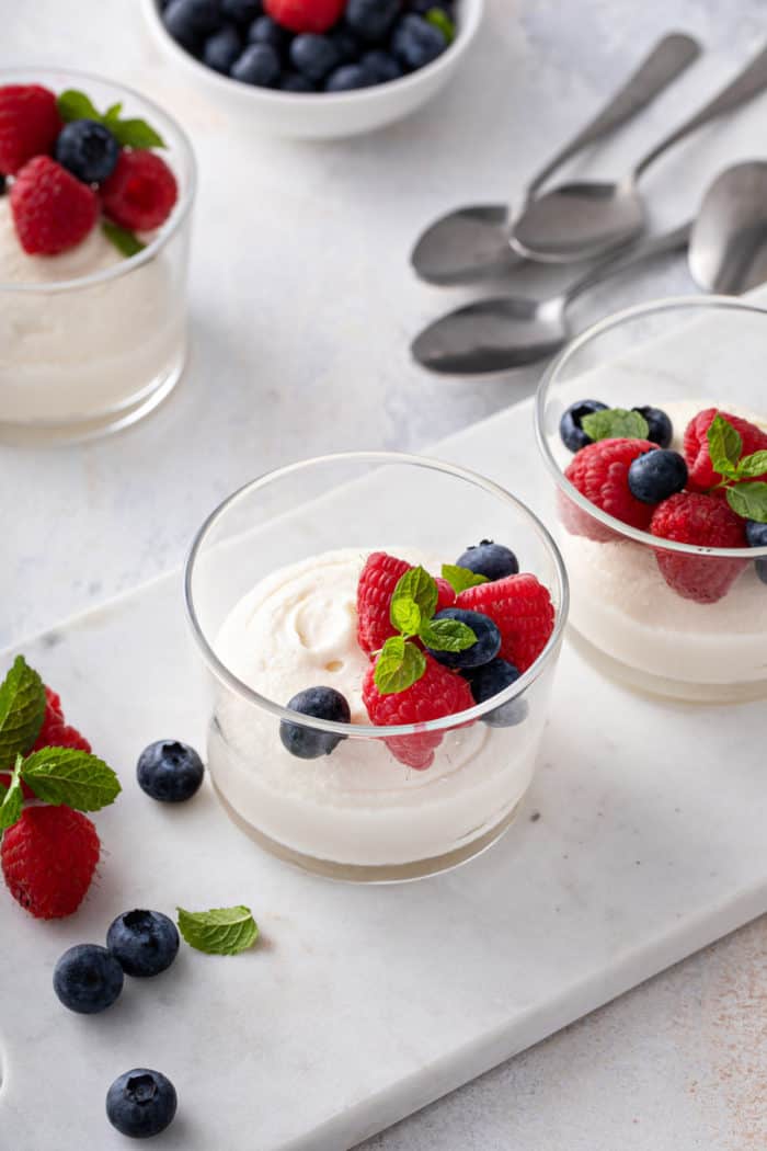 Glass dishes of white chocolate mousse, each topped with fresh berries, arranged on a marble slab.