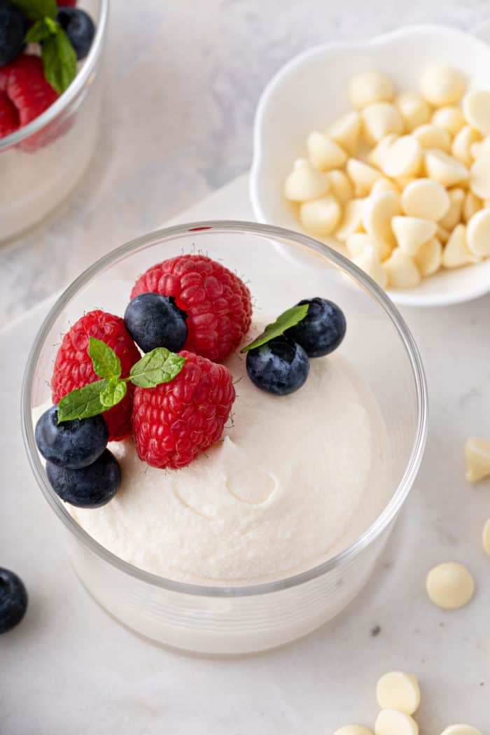 Close up of white chocolate mousse in a glass bowl, topped with fresh berries and a sprig of mint.