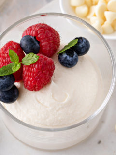 Close up of white chocolate mousse in a glass bowl, topped with berries.