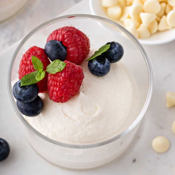 Close up of white chocolate mousse in a glass bowl, topped with berries.