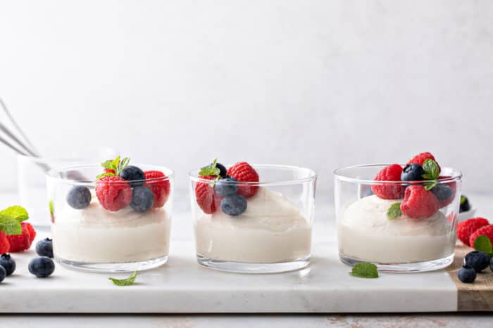 Three glass dishes of white chocolate mousse, topped with berries, lined up on a platter.