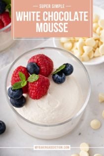 Close up of white chocolate mousse in a glass bowl, topped with fresh berries and a sprig of mint. Text overlay includes recipe name.