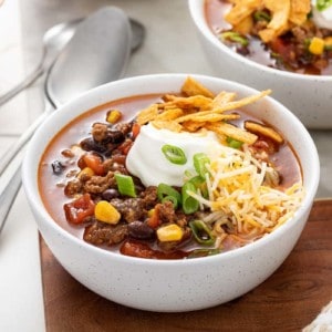 White bowl filled with taco soup and garnished with sour cream and cheese and tortilla strips