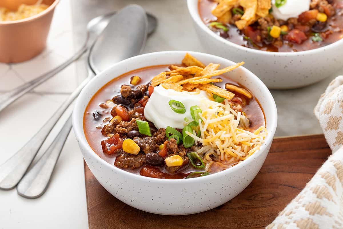 White bowl filled with taco soup and garnished with sour cream and cheese and tortilla strips