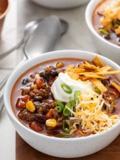 Close up of a white bowl filled with taco soup, garnished with sour cream, cheese, and tortilla strips
