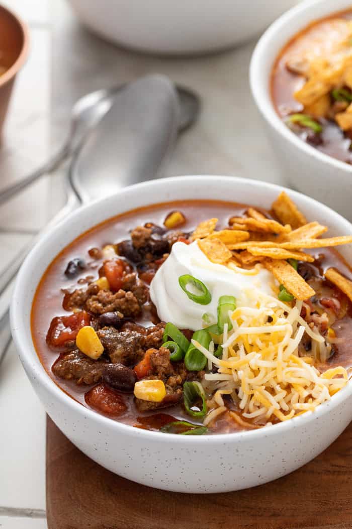 Close up of a white bowl filled with taco soup, garnished with sour cream, cheese, and tortilla strips