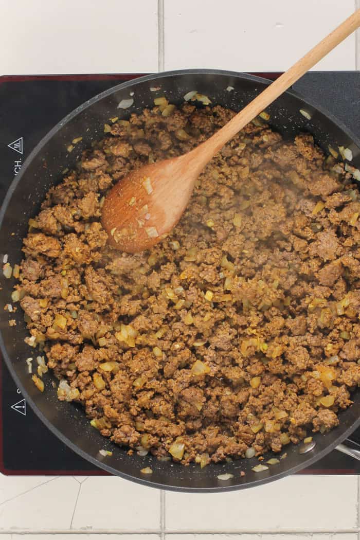 Cooked taco meat in a skillet, being stirred with a wooden spoon