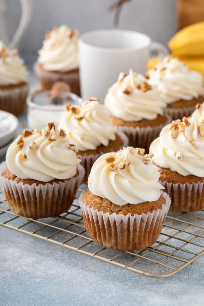 Frosted banana cupcakes, garnished with chopped pecans, set on a wire cooling rack