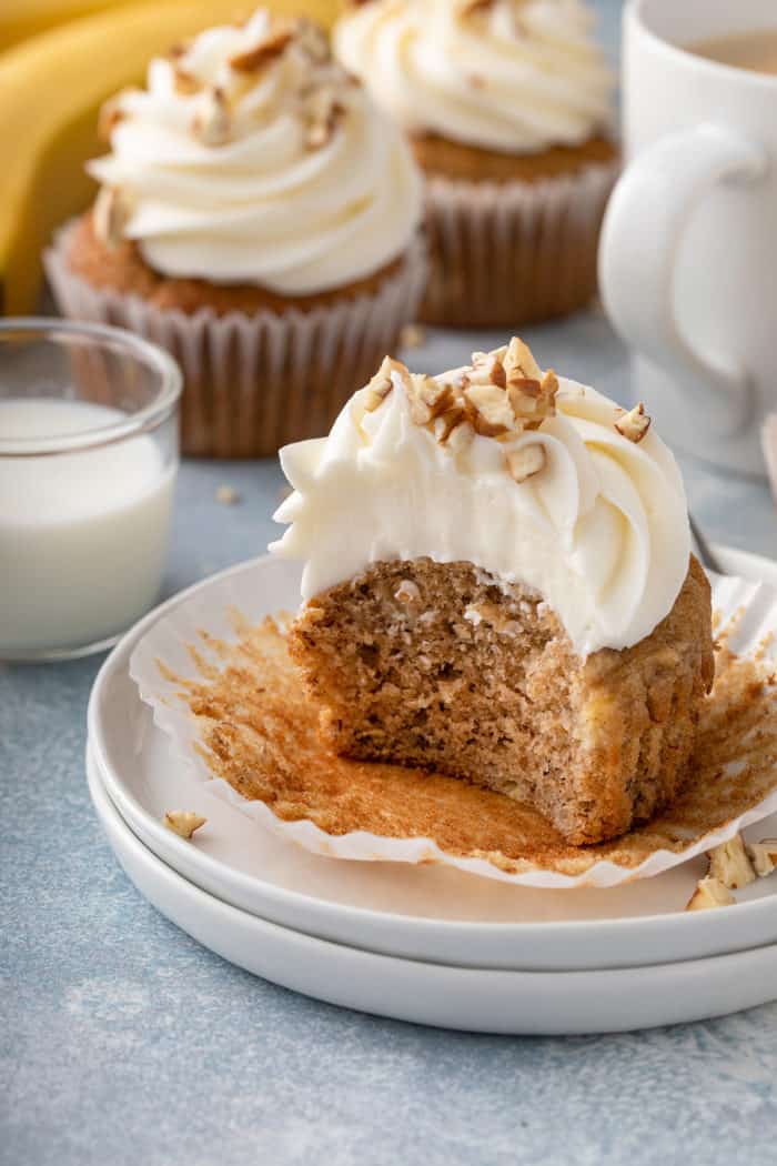 Half-eaten banana cupcake set on a white plate. More cupcakes are in the background