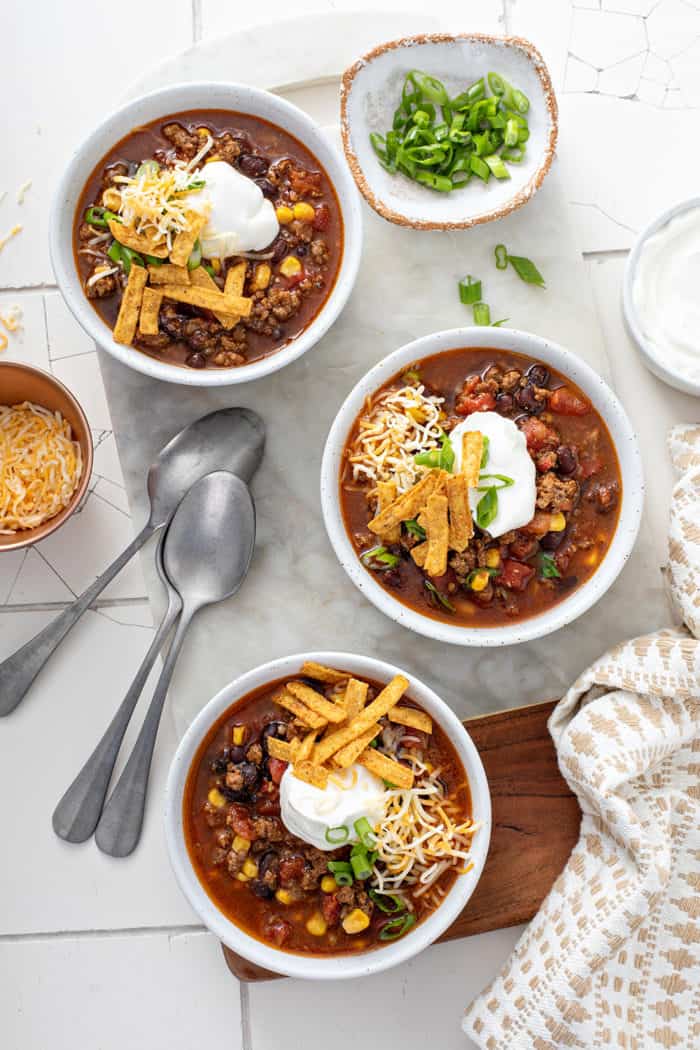 Overhead view of three bowls of taco soup, topped with sour cream, cheese, and tortilla strips