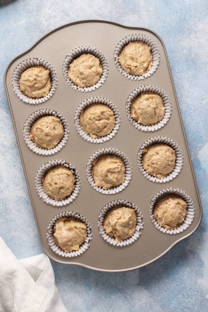 Cupcake batter divided into muffin cups, set on a blue countertop