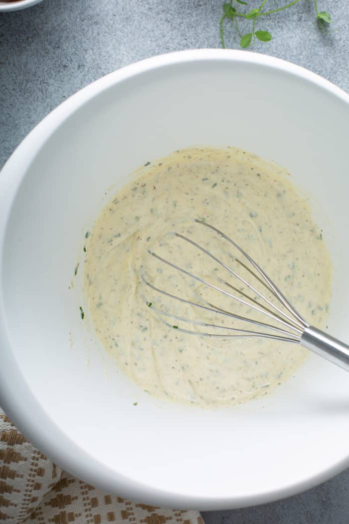 Whisk stirring together dressing for Amish Pea Salad in a white mixing bowl