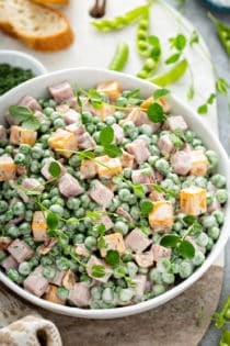 Close up of a bowl of Amish Pea Salad garnished with fresh herbs