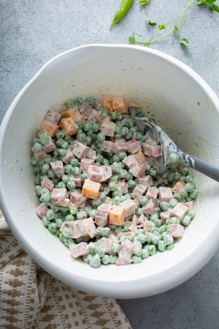 Spatula stirring together Amish pea salad in a white mixing bowl