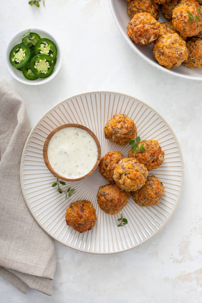 Overhead view of several sausage balls arranged on a white plate next to a bowl of ranch dip
