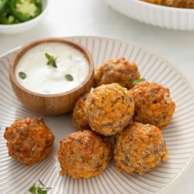 Several sausage balls arranged on a white plate next to a bowl of ranch