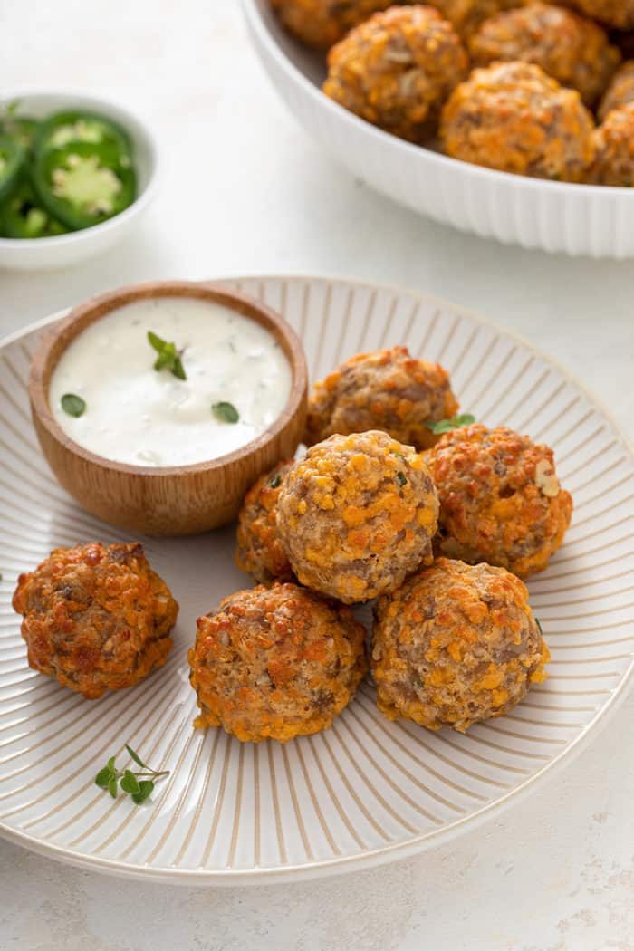 Several sausage balls arranged on a white plate next to a bowl of ranch