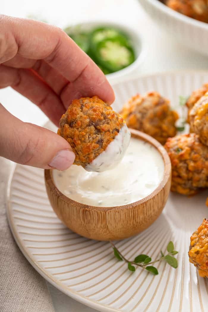 Hand dipping a sausage ball in ranch dressing