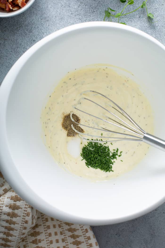 Whisk about to stir together the ingredients for pea salad dressing in a white mixing bowl