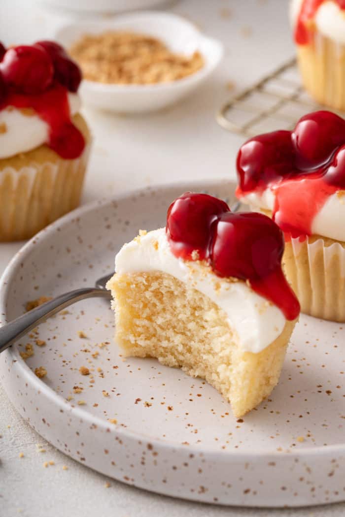 Bite taken from a cherry cheesecake cupcake on a speckled plate.