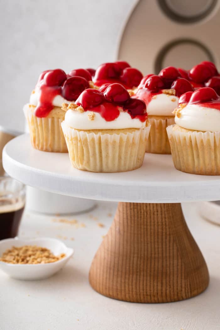 Cherry cheesecake cupcakes on a white cake stand.