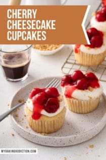 Two cherry cheesecake cupcakes next to a fork on a speckled plate. Text overlay includes recipe name.