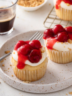 Two cherry cheesecake cupcakes on a speckled plate.