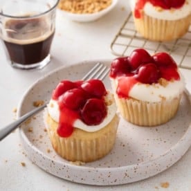Two cherry cheesecake cupcakes on a speckled plate.