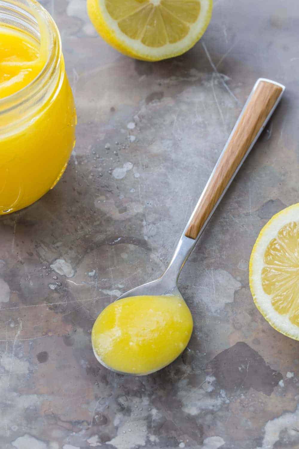 Spoon full of lemon curd next to cut lemons