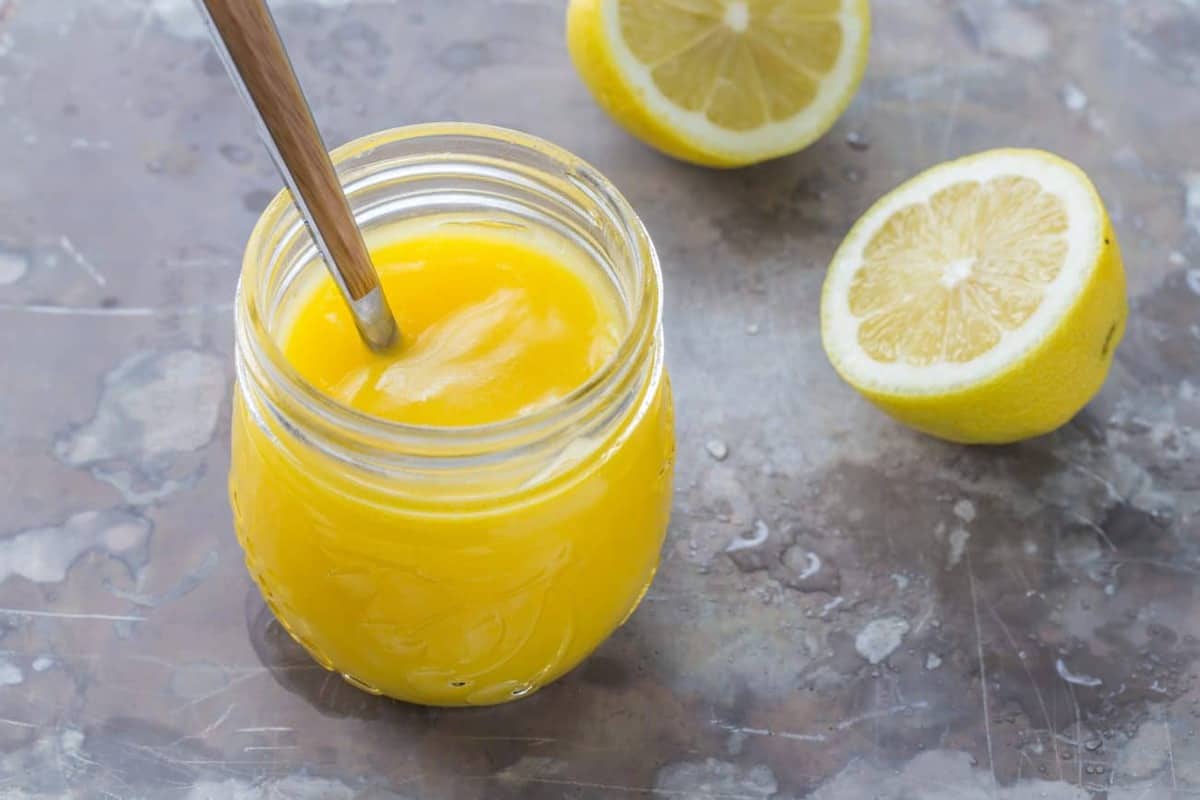 Jar of lemon curd with a spoon next to cut lemons