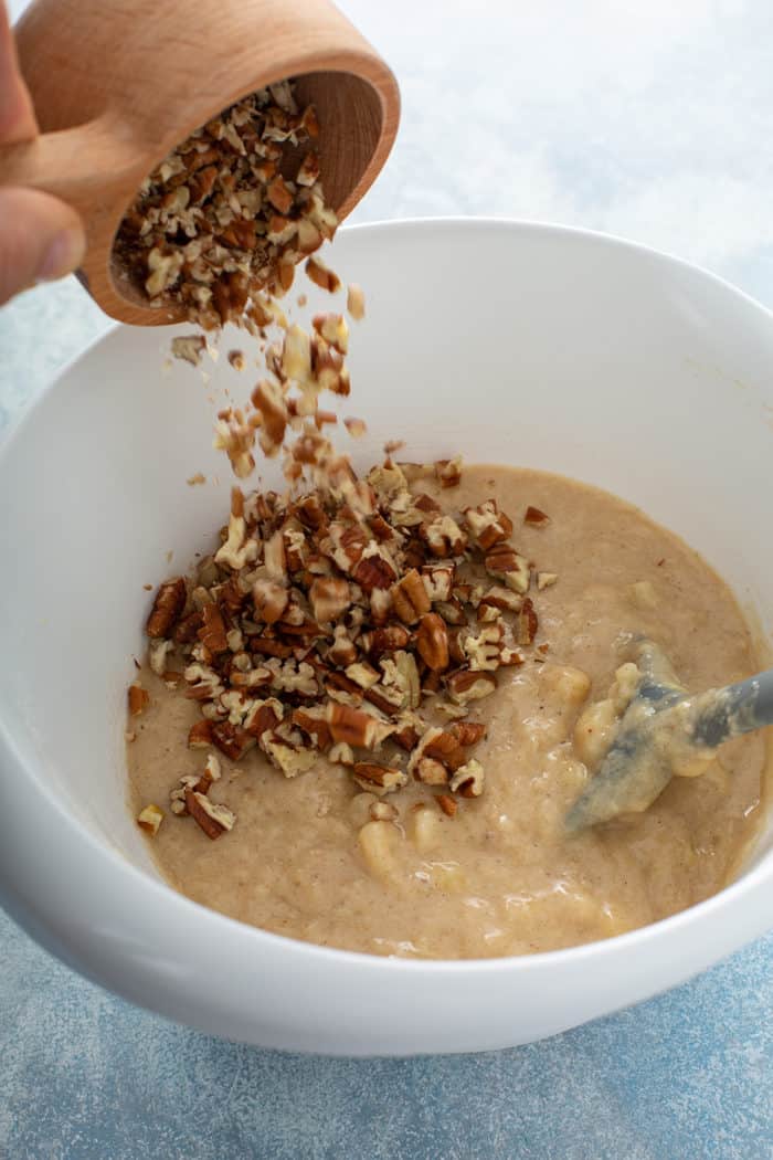 Chopped pecans being added to hummingbird cupcake batter in a white bowl