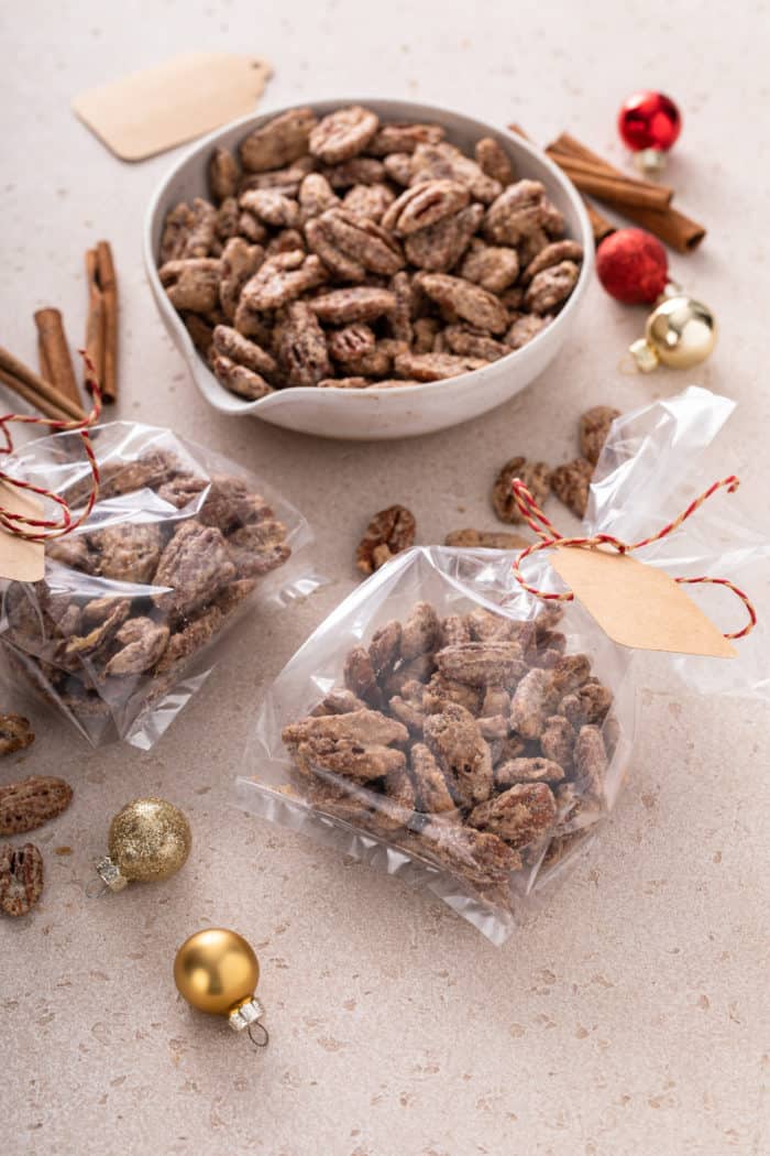 Candied pecans packaged in two small plastic gift bags on a counter in front of a bowl of candied pecans.