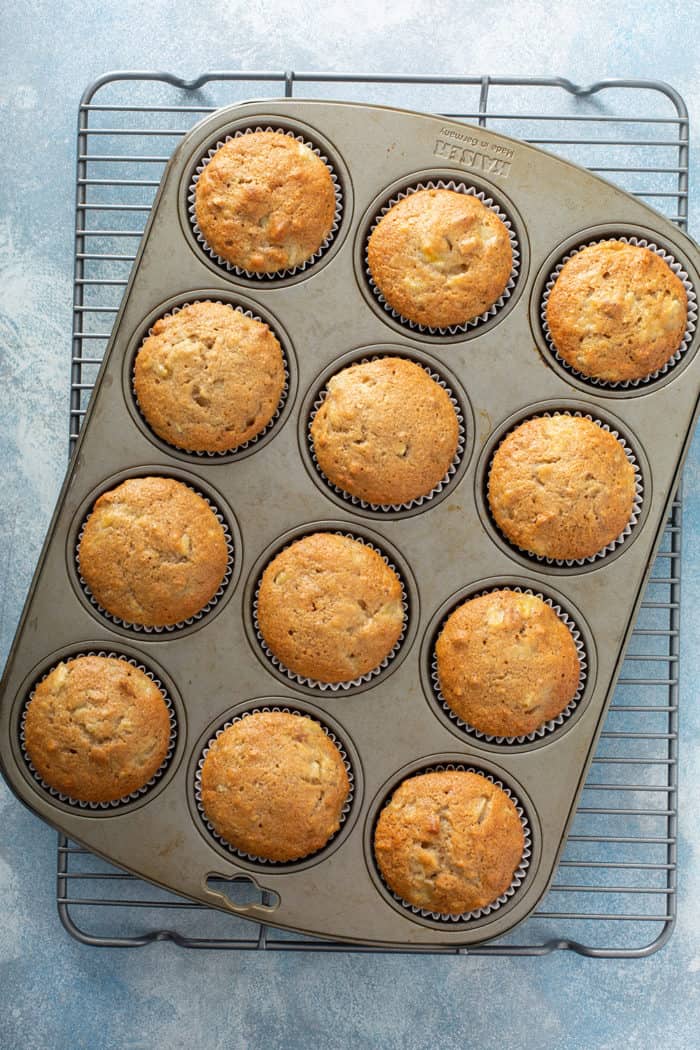 Baked hummingbird cupcakes in a muffin tin, set on a wire cooling rack