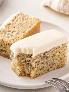 Halved slice of banana cake on a plate with a bite taken from the corner.