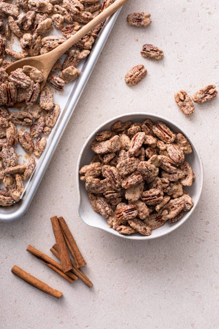 Overhead view of candied pecans in a bowl next to a baking sheet of candied pecans.