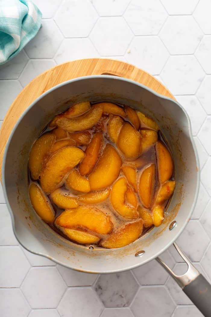 Peach compote in a saucepan set on a wooden trivet