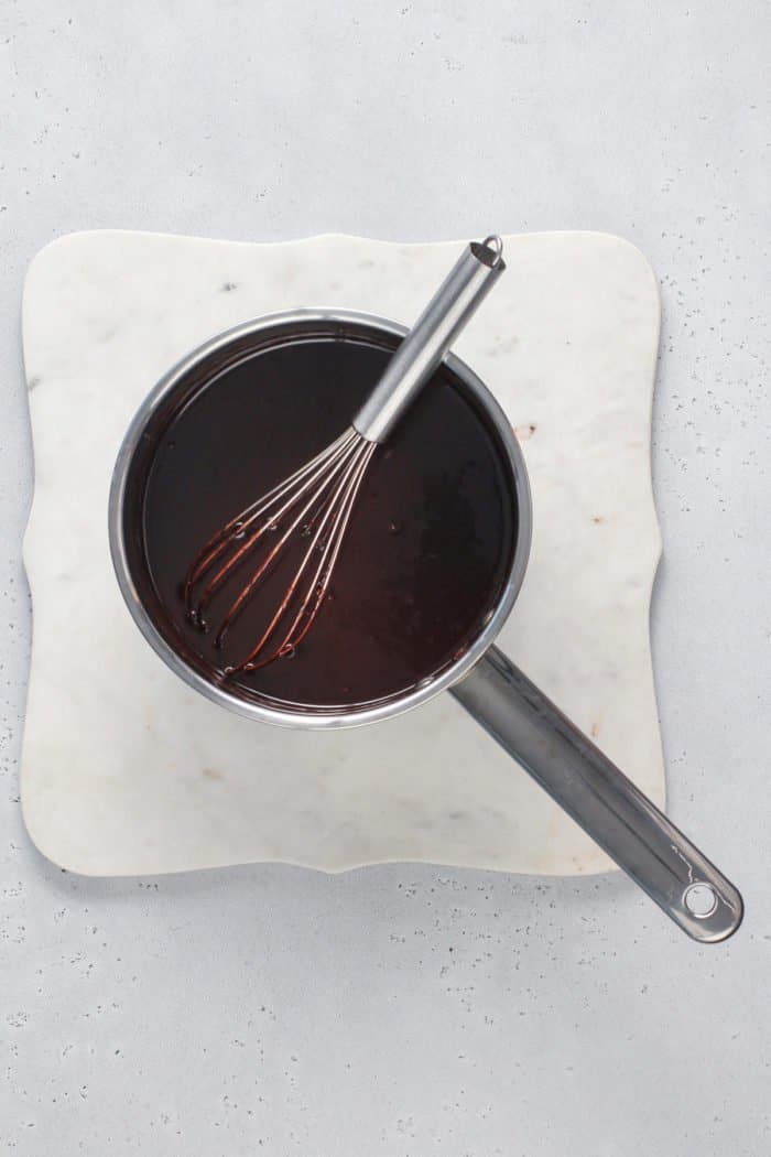 Saucepan of hot fudge sauce cooling on a white board.