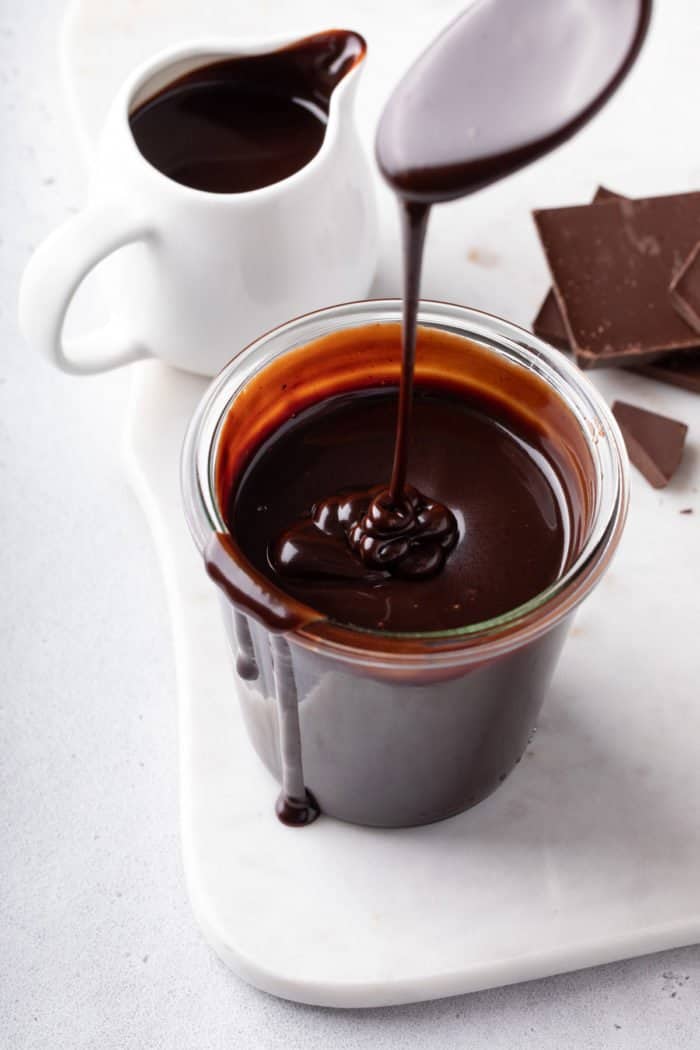 Spoon drizzling hot fudge sauce back into a jar of the sauce.