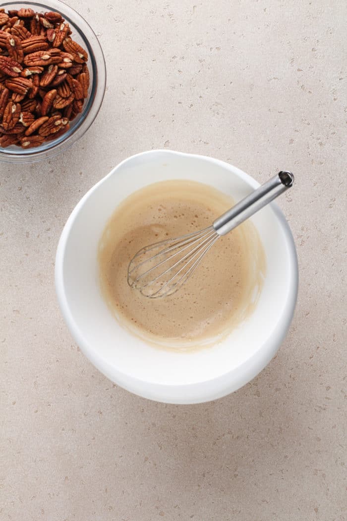 Frothy egg whites and vanilla whisked in a white mixing bowl.