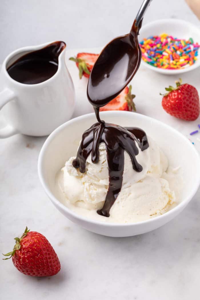 Hot fudge sauce being drizzled over vanilla ice cream in a white bowl.